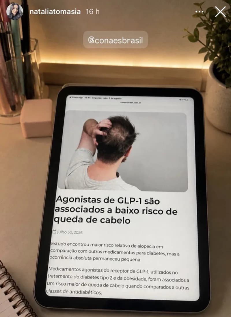 Story de @nataliatomasia lendo no tablet a matéria do CONAES sobre agonistas de GLP-1 e risco de queda de cabelo